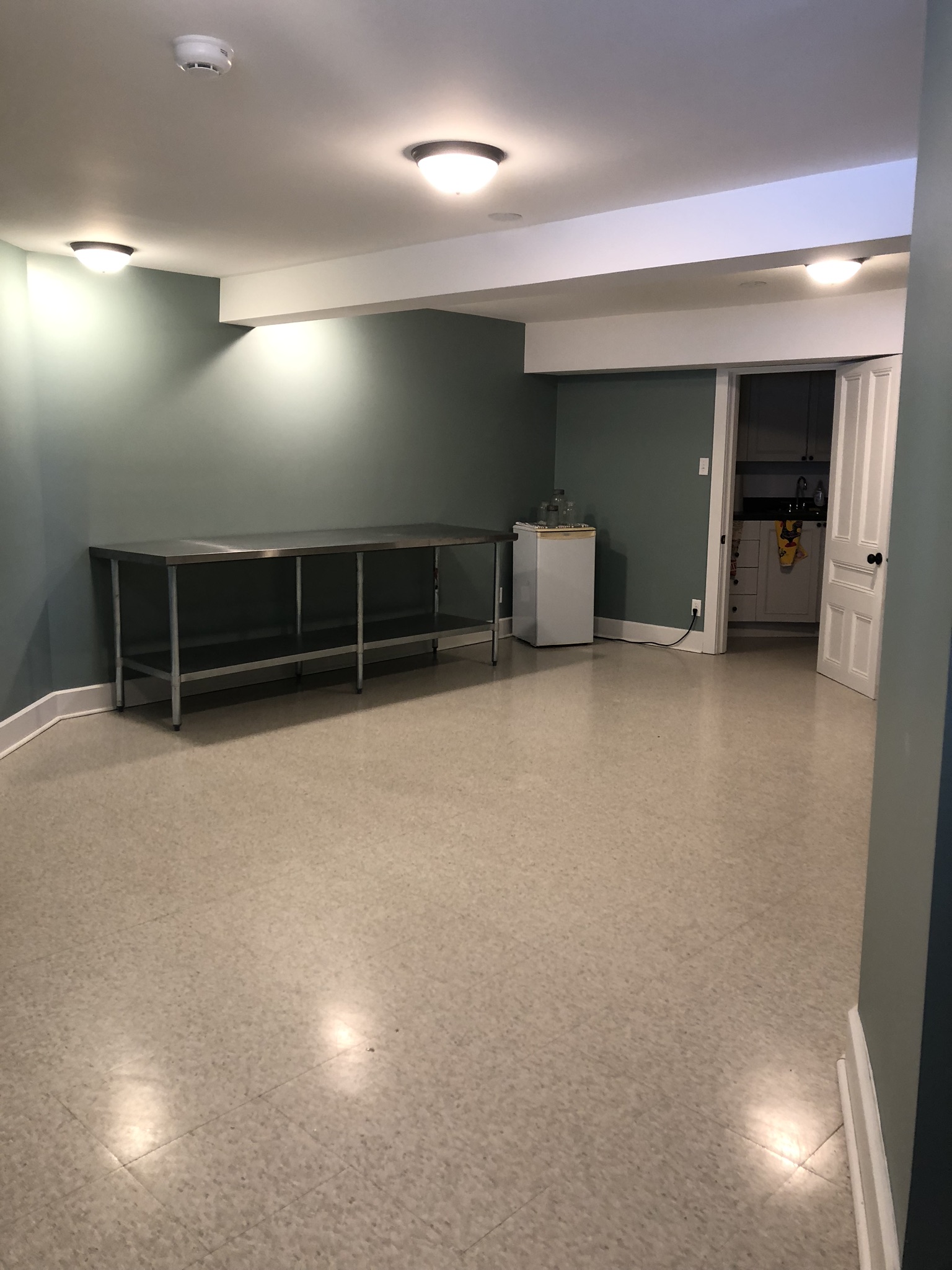 Image of basement room with stainless steel table and mini fridge.